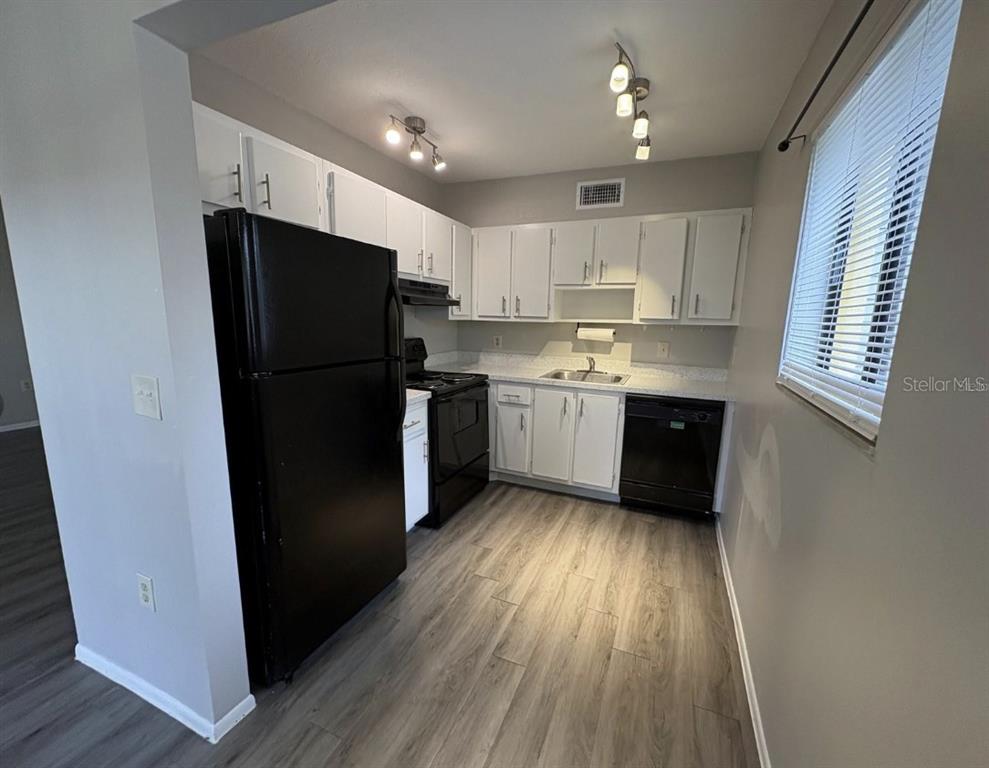 A kitchen features white cabinets, black appliances, and light wood-look flooring — 2683 OAK PARK WAY UNIT 214, ORLANDO, FL