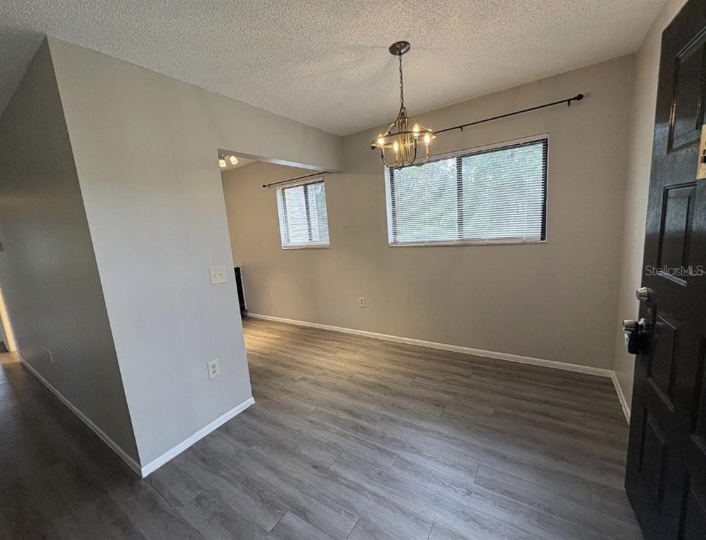 An empty room with gray wood-look flooring, light gray walls, and a hanging chandelier — 2683 OAK PARK WAY UNIT 214, ORLANDO, FL