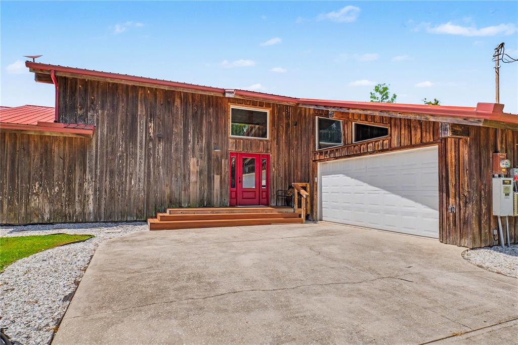 A rustic wood-sided house features a red front door, metal roof, and attached white garage — 153897 COUNTY ROAD 108, YULEE, FL