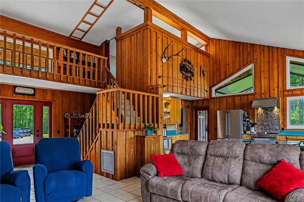 A rustic living room features wood-paneled walls, a loft area, and a staircase — 153897 COUNTY ROAD 108, YULEE, FL
