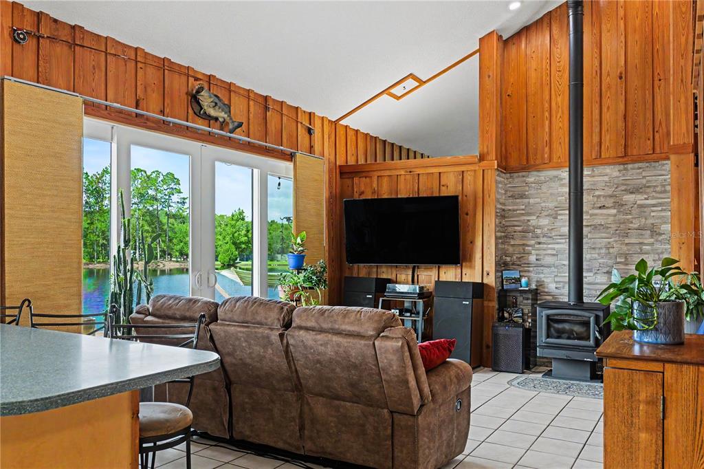 A living room features wood-paneled walls, a stone fireplace, a television, and views of water — 153897 COUNTY ROAD 108, YULEE, FL