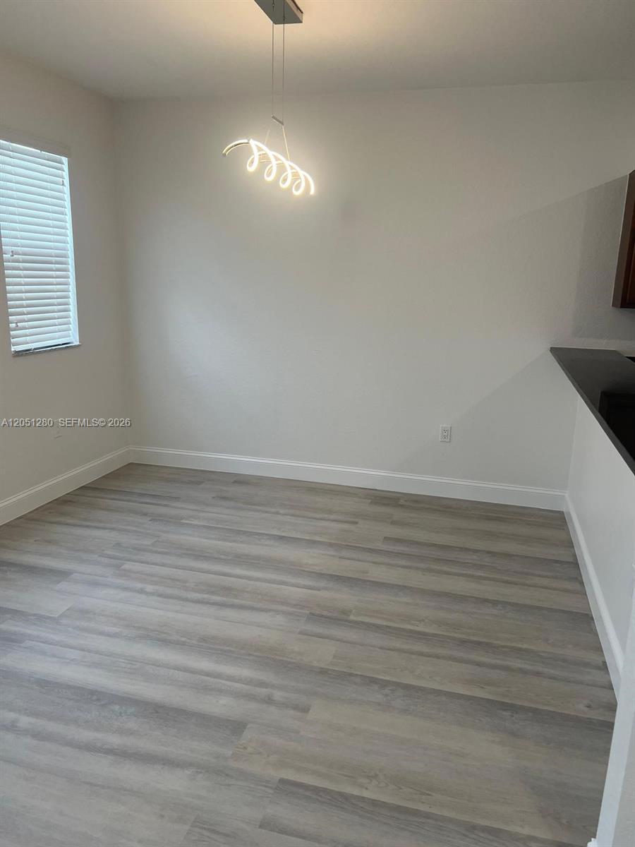 This dining area features light wood-look flooring, white walls, and a modern spiral pendant light — 8760 NW 97th Ave # 205, Doral FL 33178, DORAL, FL