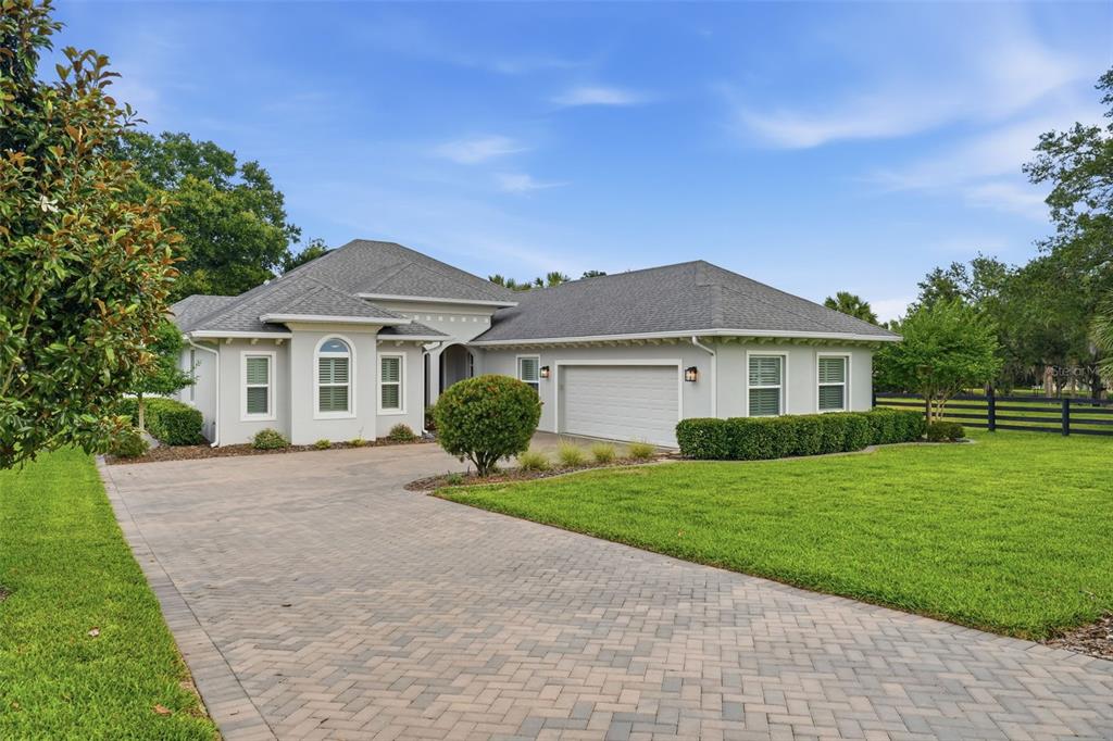 A single-story house with a gray roof, light-colored stucco walls, and a paved driveway — 5066 GREENS DRIVE, LADY LAKE, FL