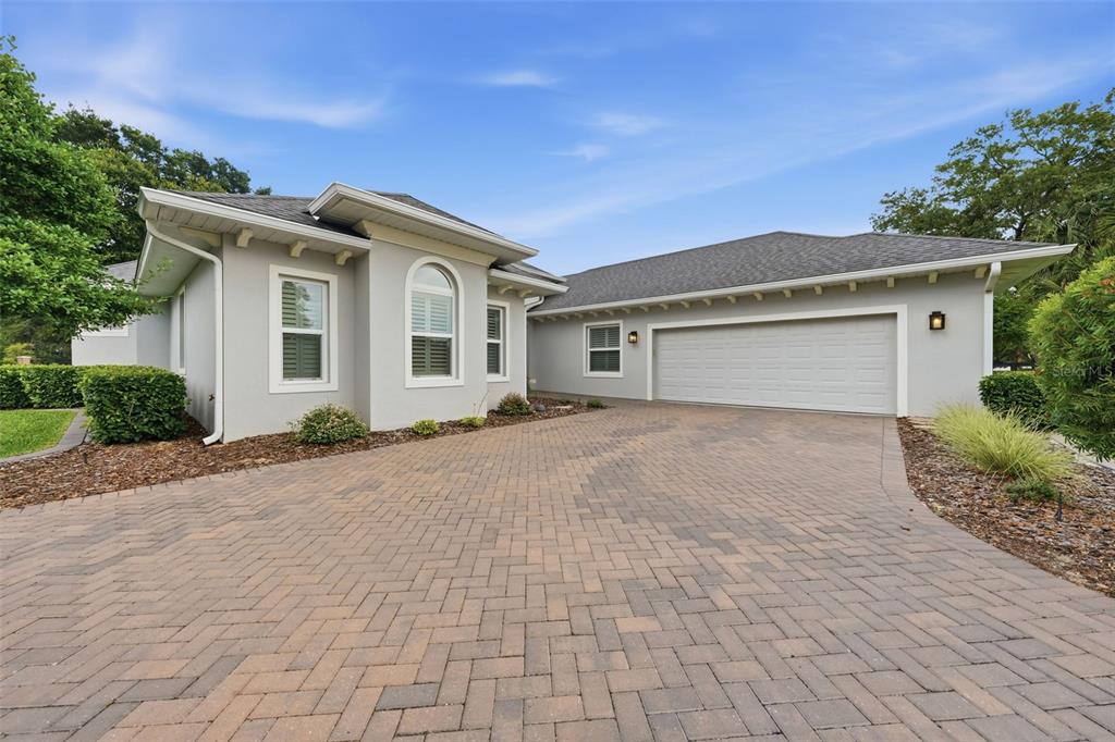 A gray house with a paved driveway and a two-car garage under a blue sky — 5066 GREENS DRIVE, LADY LAKE, FL