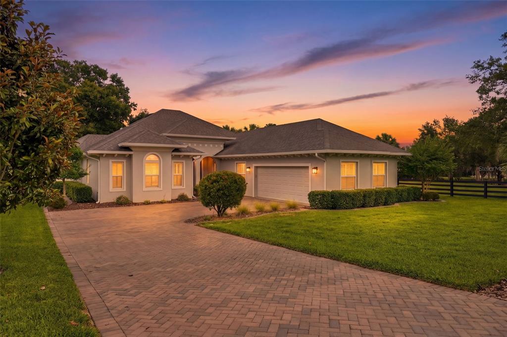A single-story house with a paved driveway, a two-car garage, and a sunset sky — 5066 GREENS DRIVE, LADY LAKE, FL