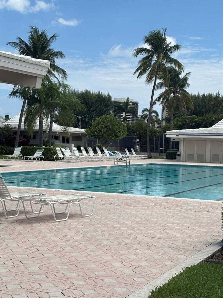 A swimming pool surrounded by lounge chairs, palm trees, and buildings under a blue sky — 1260 Sugar Sands Boulevard # 206, Singer Island FL 33404, SINGER ISLAND, FL