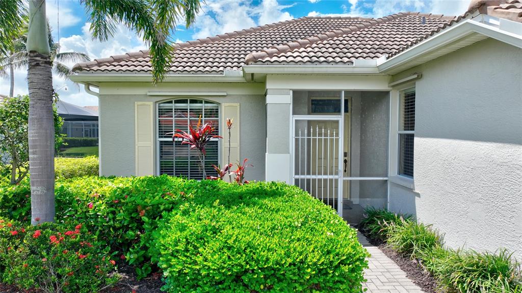 The exterior of a single-story house features a tiled roof, a screened entryway, and landscaping — 17900 COURTSIDE LANDINGS CIRCLE, PUNTA GORDA, FL