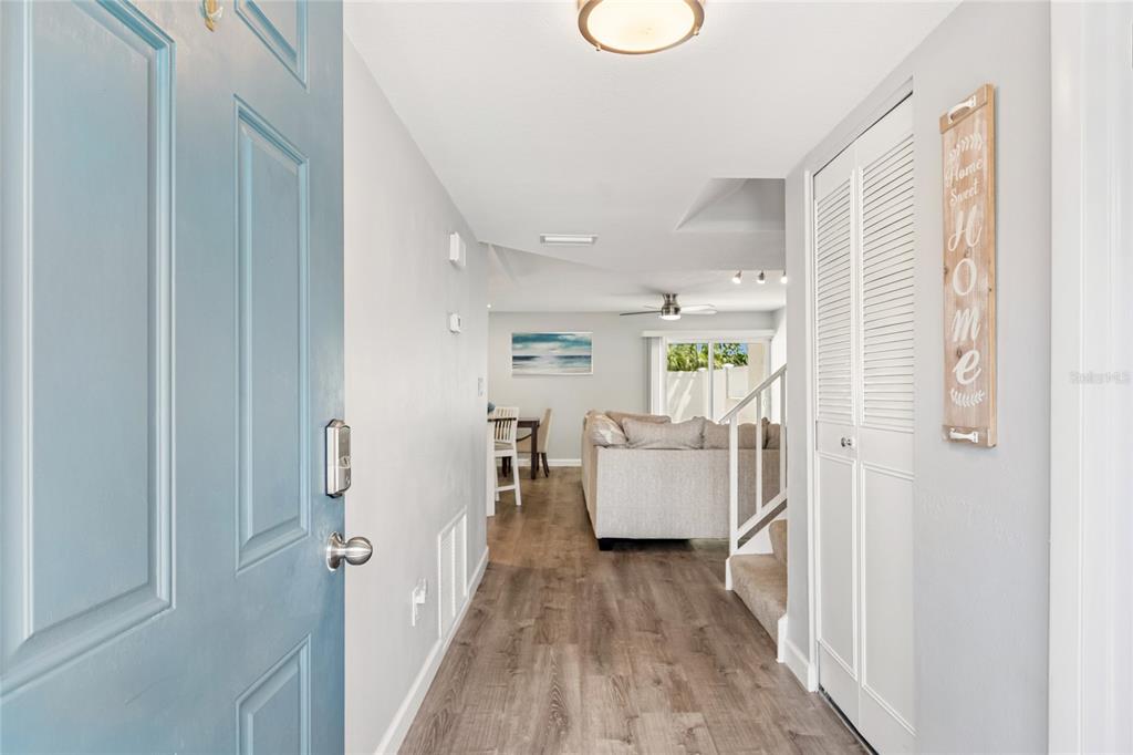 An entryway with wood-look flooring leads into a living room with a staircase and sofa — 7324 STONE HAVEN COURT N, PINELLAS PARK, FL
