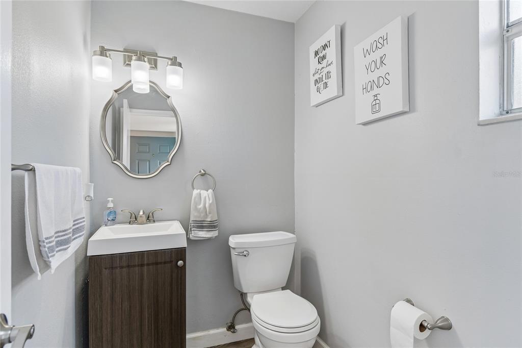 A small bathroom features a pedestal vanity, a round mirror, and a white toilet — 7324 STONE HAVEN COURT N, PINELLAS PARK, FL