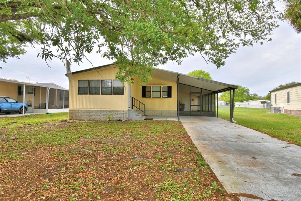 A yellow single-story mobile home features a concrete driveway, a carport, and a screened porch — 2737 CRANMOOR DRIVE, KISSIMMEE, FL
