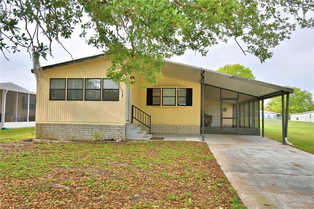 A yellow mobile home features a concrete driveway, a screened-in porch, and a brick base — 2737 CRANMOOR DRIVE, KISSIMMEE, FL