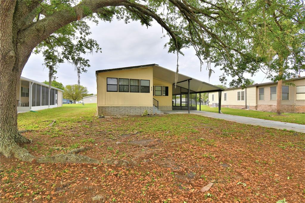 A yellow mobile home with a carport and a large oak tree in the yard — 2737 CRANMOOR DRIVE, KISSIMMEE, FL