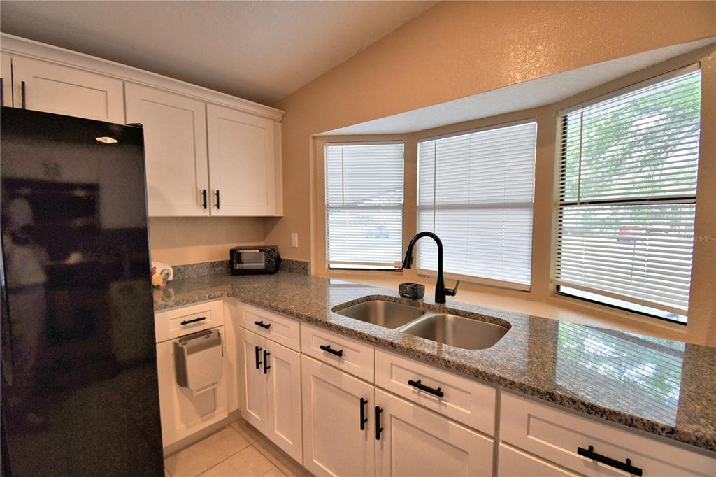 A kitchen features white cabinets, granite countertops, a double sink, and a black refrigerator — 2737 CRANMOOR DRIVE, KISSIMMEE, FL