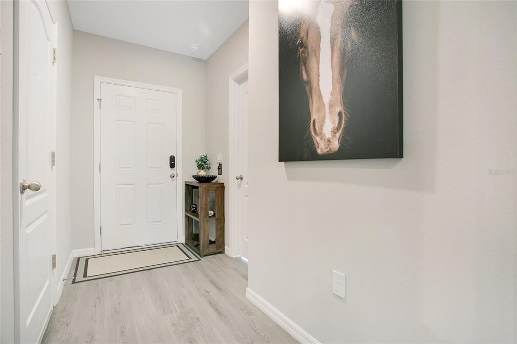 An entryway features light wood-look flooring, a white front door, and a horse wall art piece — 14257 SW 60TH TERRACE UNIT 1, OCALA, FL