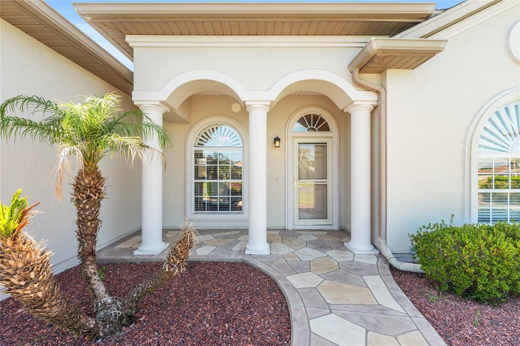 The exterior of a house features a stone walkway, three white columns, and arched windows — 10990 SE 170TH STREET ROAD, SUMMERFIELD, FL