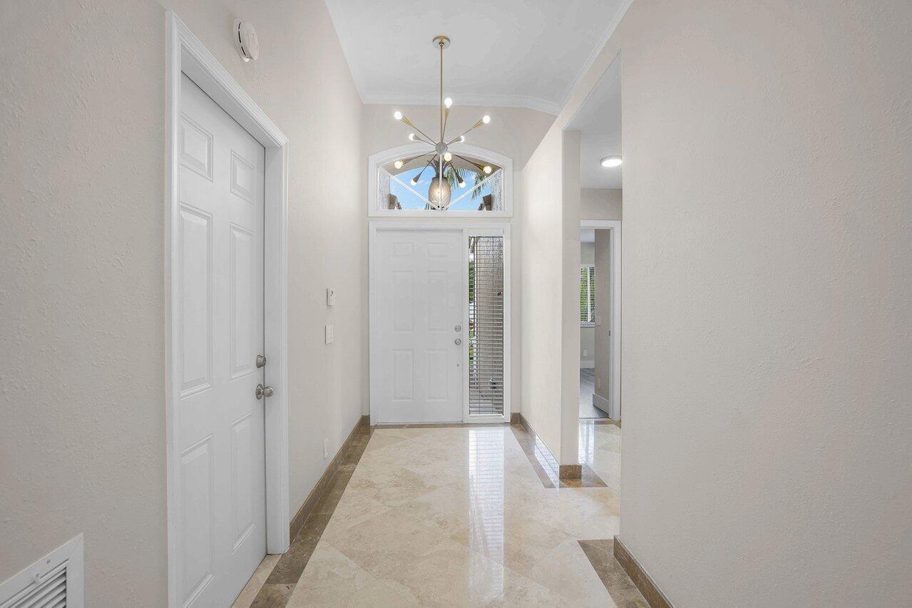 A bright entryway features a white front door, a modern chandelier, and polished tile flooring — 660 NW 45th Avenue, Deerfield Beach FL 33442, DEERFIELD BEACH, FL