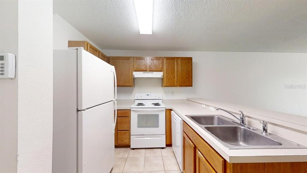 A kitchen features white appliances, wood cabinets, a double sink, and light-colored tile flooring — 4121 WINDING RIVER WAY, LAND O LAKES, FL