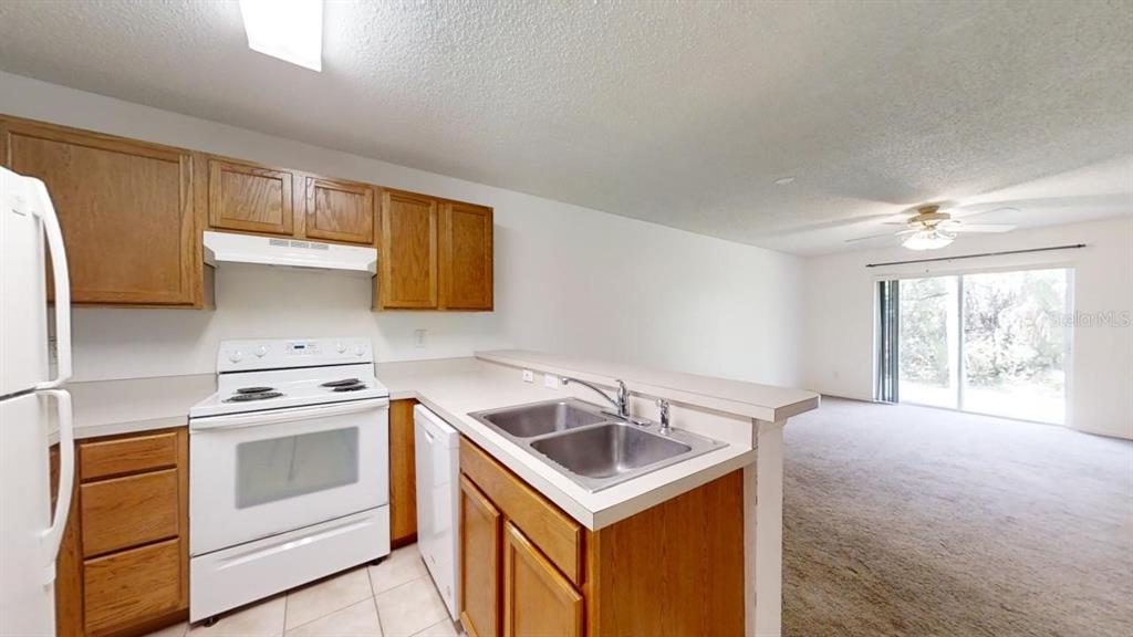 A kitchen with wood cabinets, white appliances, and a double sink overlooks a carpeted living area — 4121 WINDING RIVER WAY, LAND O LAKES, FL
