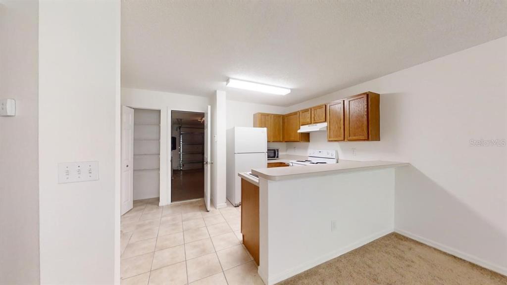 A kitchen with wood cabinets, white appliances, and a breakfast bar overlooks a carpeted area — 4121 WINDING RIVER WAY, LAND O LAKES, FL