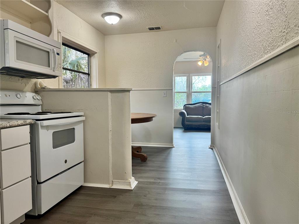 A kitchen with white appliances and wood-look flooring opens into a living area with an archway — 425 E SESSOMS AVENUE, LAKE WALES, FL