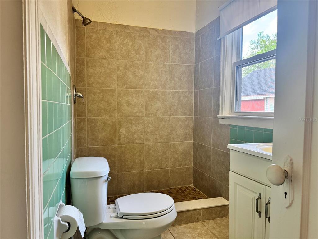 A bathroom features a walk-in shower with tan tiles, a toilet, and a green-tiled wall — 425 E SESSOMS AVENUE, LAKE WALES, FL