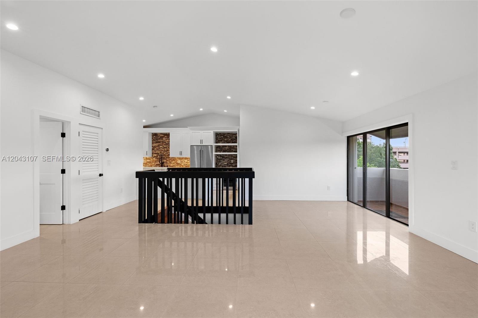 A bright, open-concept living area features white walls, glossy tile floors, and a black railing — 9001 SW 94th St # 201, Miami FL 33176, MIAMI, FL