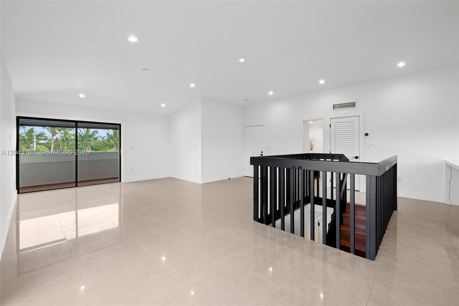 A bright, minimalist room features light tile floors, a black staircase railing, and a balcony — 9001 SW 94th St # 201, Miami FL 33176, MIAMI, FL
