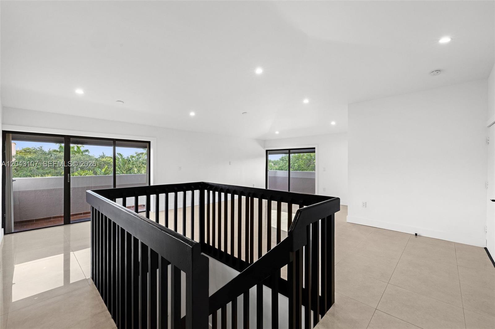 An open loft area features white walls, tile flooring, a black railing, and sliding glass doors — 9001 SW 94th St # 201, Miami FL 33176, MIAMI, FL