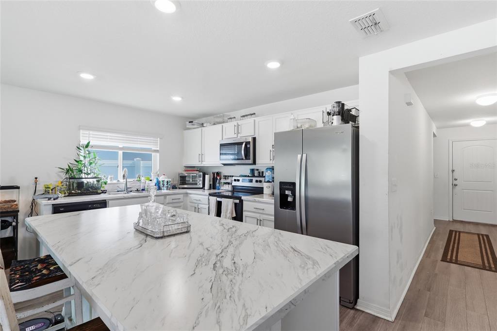 A kitchen features white cabinets, stainless steel appliances, and a large marble-patterned island countertop — 1341 MATTIE POINTE BOULEVARD, AUBURNDALE, FL