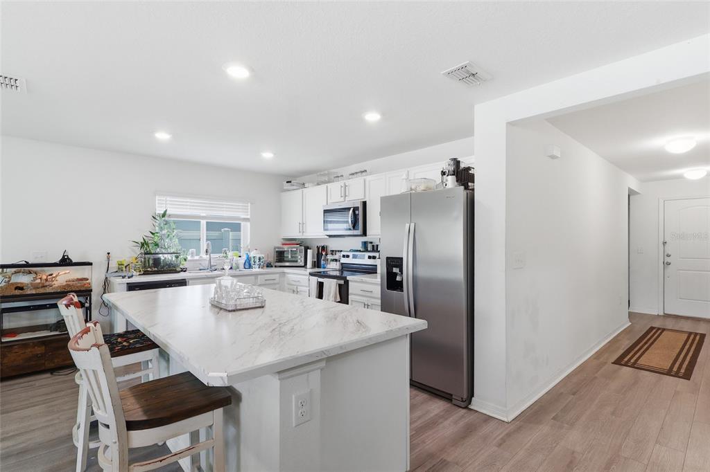 A kitchen features a marble-topped island, white cabinetry, stainless steel appliances, and light wood flooring — 1341 MATTIE POINTE BOULEVARD, AUBURNDALE, FL