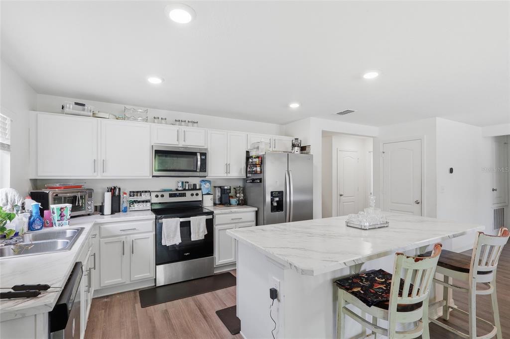 A kitchen features white cabinets, stainless steel appliances, and a marble-topped island with seating — 1341 MATTIE POINTE BOULEVARD, AUBURNDALE, FL