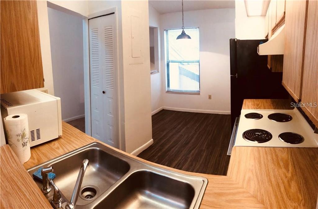 A kitchen features wood-look cabinets, a double sink, a white stove, and dark flooring — 3036 S SEMORAN BOULEVARD UNIT M2, ORLANDO, FL