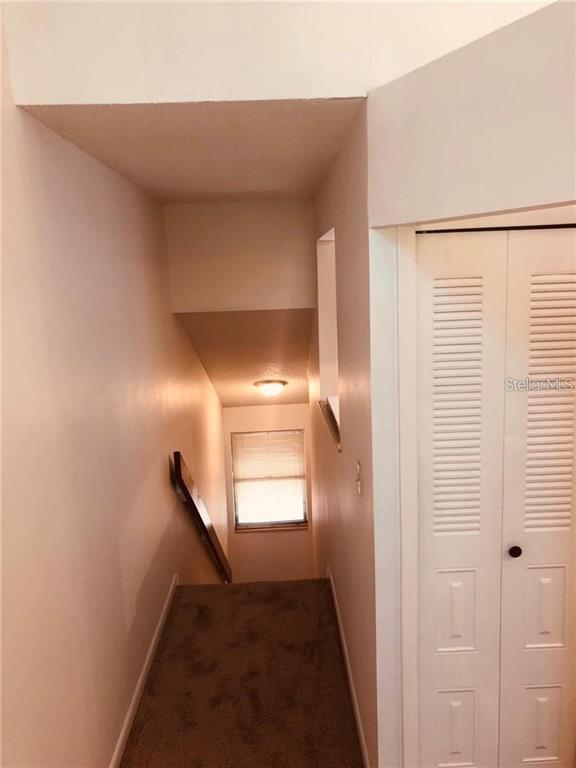 A carpeted staircase leads down to a landing with a window and a louvered closet door — 3036 S SEMORAN BOULEVARD UNIT M2, ORLANDO, FL
