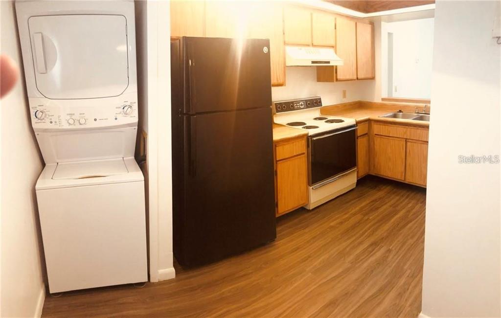 A kitchen features wood cabinets, a black refrigerator, a white stove, and a stacked laundry unit — 3036 S SEMORAN BOULEVARD UNIT M2, ORLANDO, FL