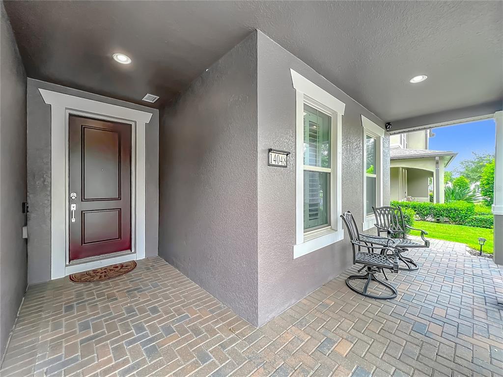 A covered brick porch features a dark front door, two metal chairs, and gray walls — 14048 LAKE ABBOTTS DRIVE, WINTER GARDEN, FL