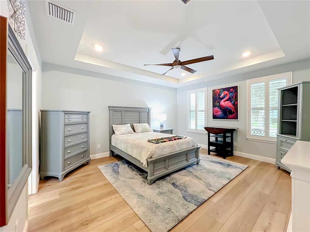 A bedroom features a tray ceiling, light wood flooring, a bed, and a flamingo wall art — 14048 LAKE ABBOTTS DRIVE, WINTER GARDEN, FL