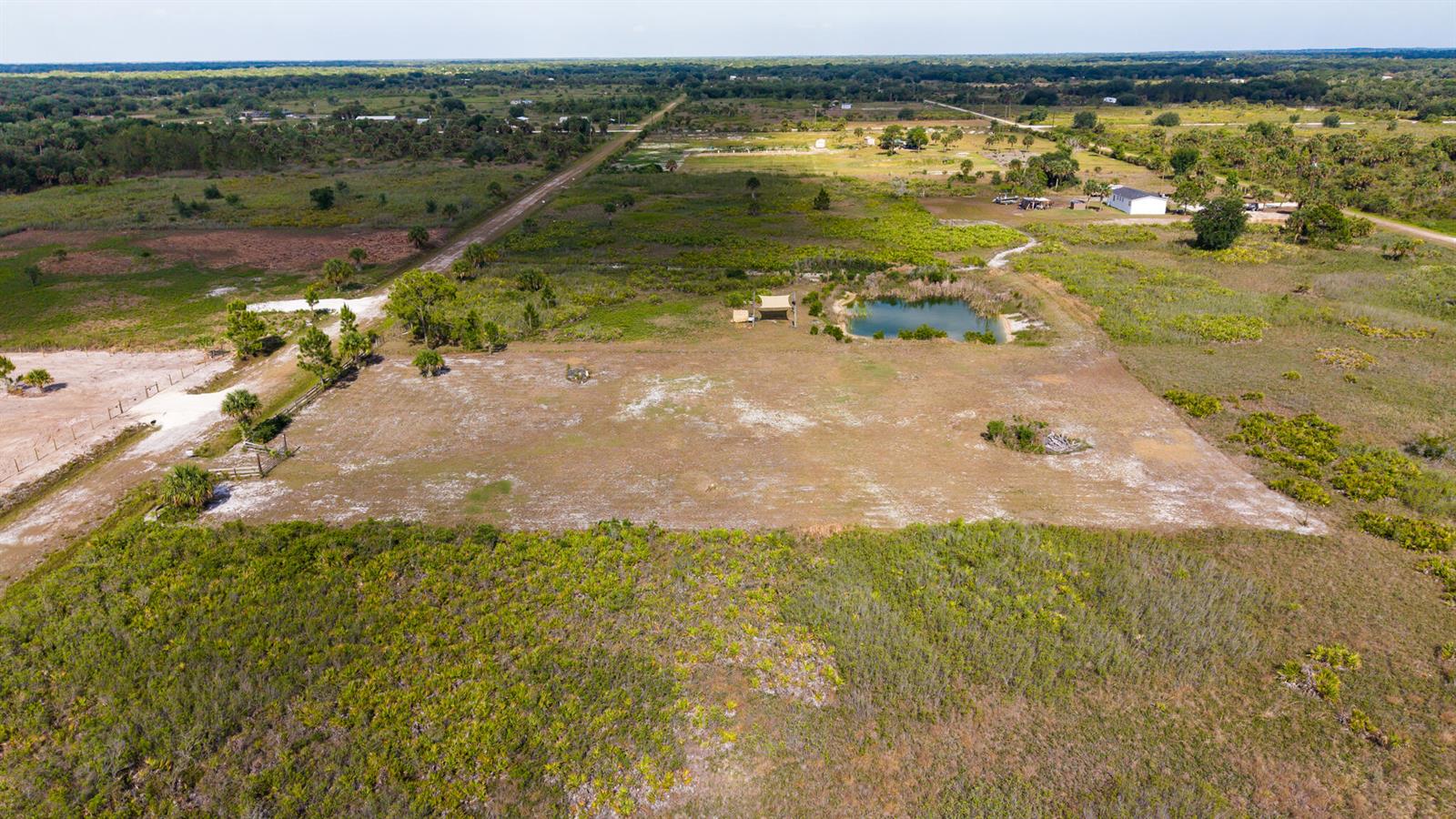 An aerial view shows a large, cleared rectangular lot with a small pond and trees — 21228 NW 280th Street, Okeechobee FL 34972, OKEECHOBEE, FL
