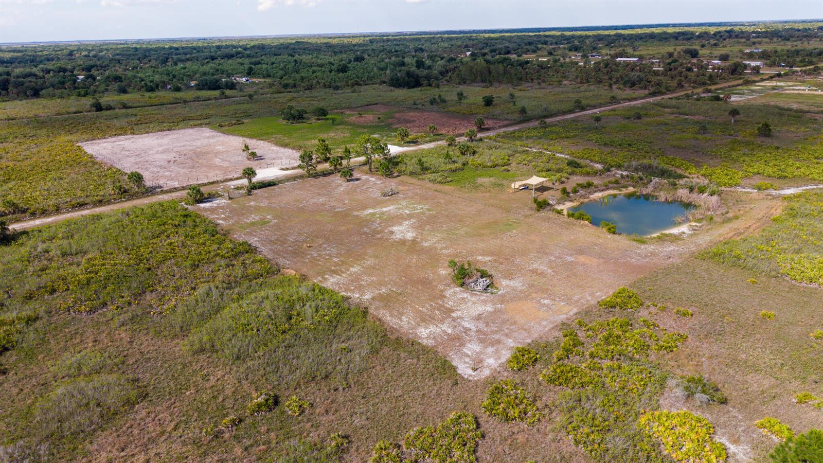 An aerial view shows a cleared rectangular lot with a small pond and shade structure — 21228 NW 280th Street, Okeechobee FL 34972, OKEECHOBEE, FL