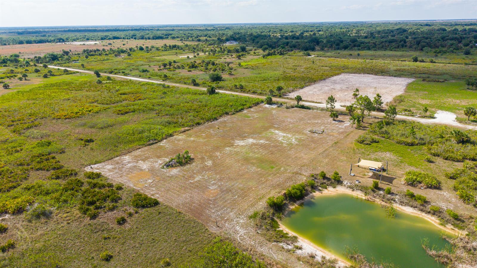 An aerial view shows a large, cleared grassy lot with a small pond and shelter — 21228 NW 280th Street, Okeechobee FL 34972, OKEECHOBEE, FL