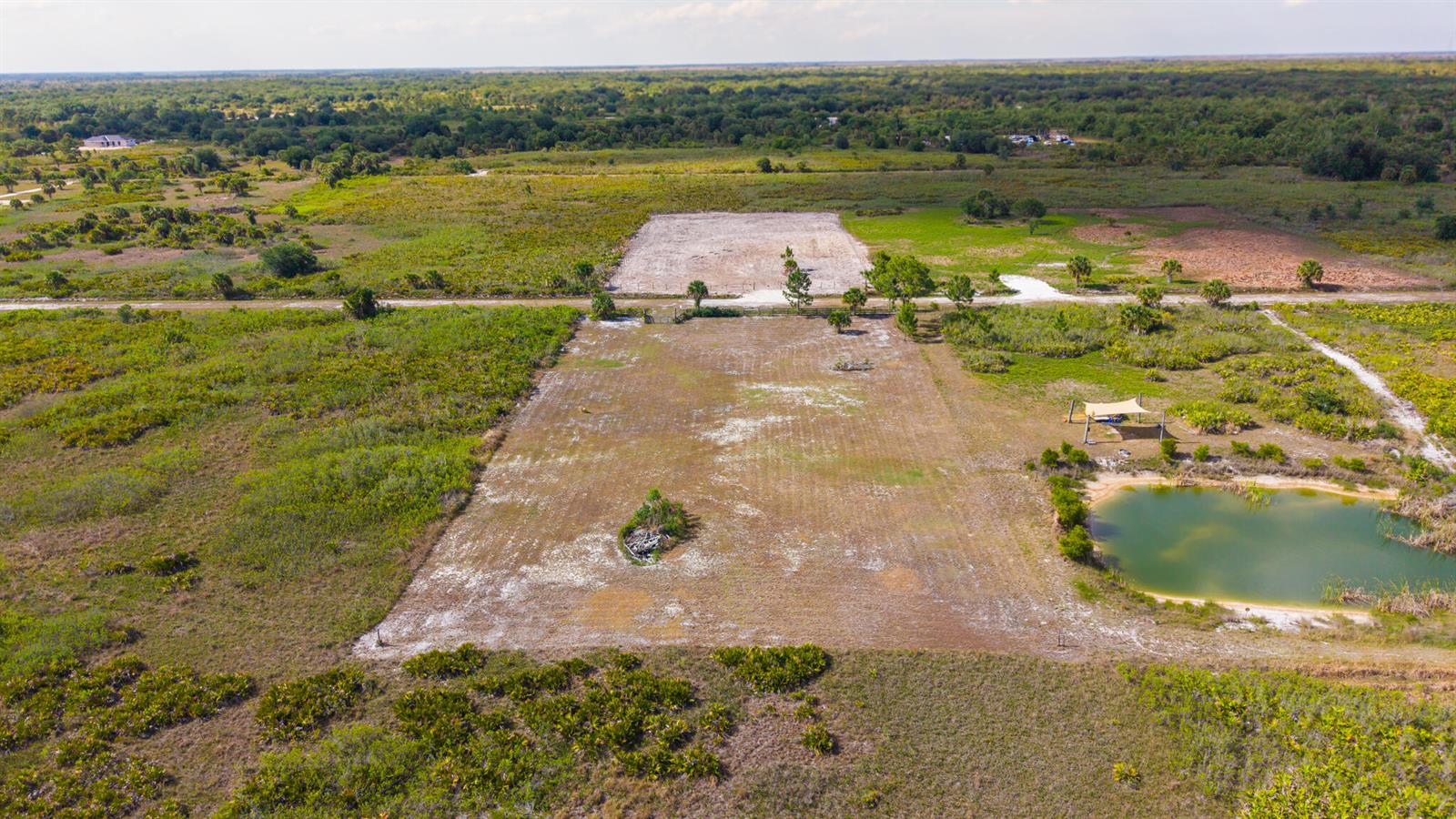 An aerial view shows a cleared rectangular plot of land featuring a small pond — 21228 NW 280th Street, Okeechobee FL 34972, OKEECHOBEE, FL