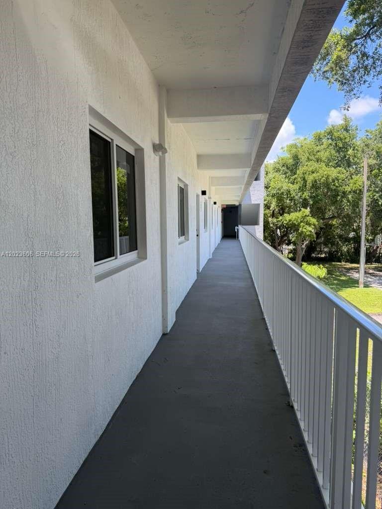 An outdoor apartment walkway features white walls, a dark floor, and a metal railing — 147 Nw 59th St # 202, Miami FL 33127, MIAMI, FL