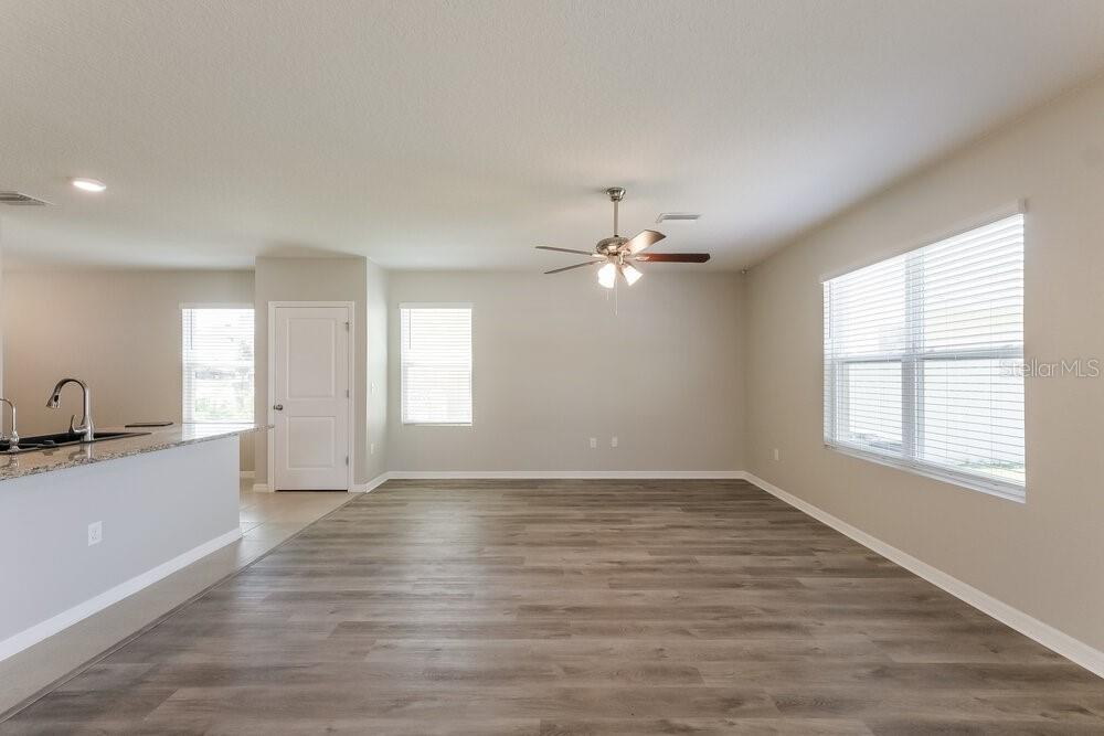 An open-concept living area features light gray walls, wood-look flooring, and a ceiling fan — 10988 CARLTON FIELDS DRIVE, RIVERVIEW, FL