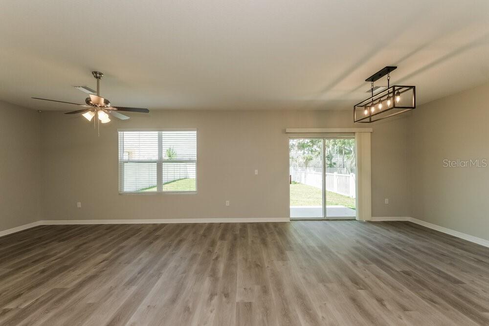 An empty living room features light gray wood-look flooring, a ceiling fan, and sliding doors — 10988 CARLTON FIELDS DRIVE, RIVERVIEW, FL