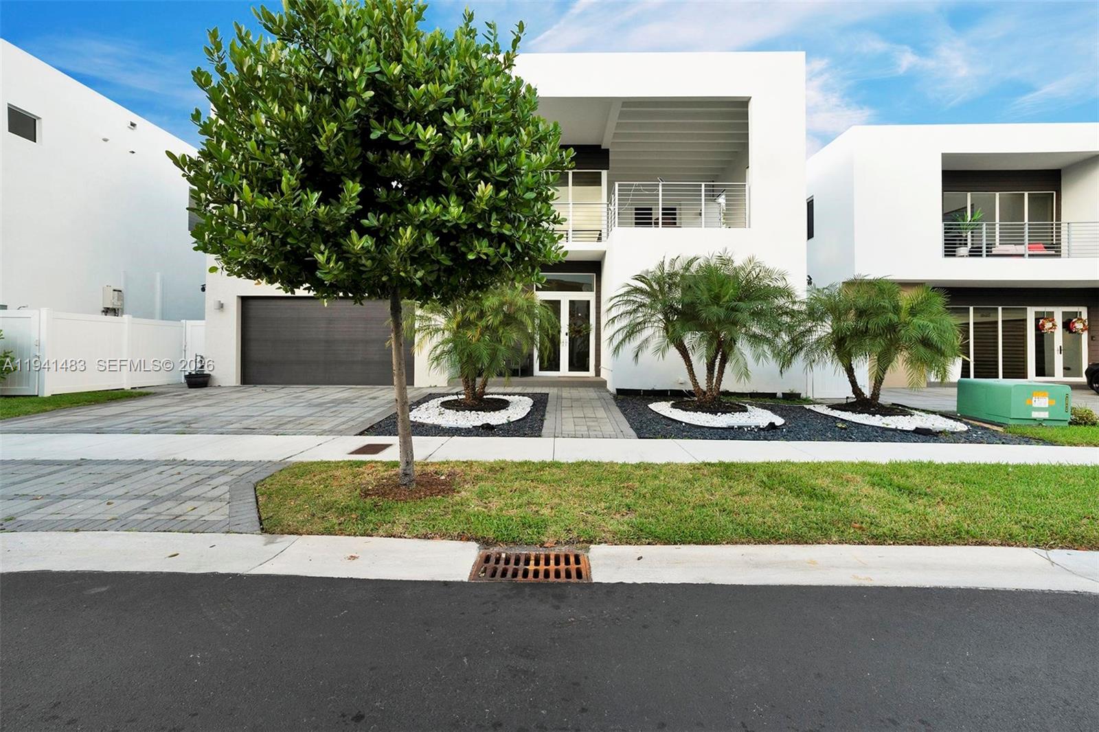 A modern white two-story house features a paved driveway, palm trees, and a garage — 10055 NW 77th St, Doral FL 33178, DORAL, FL