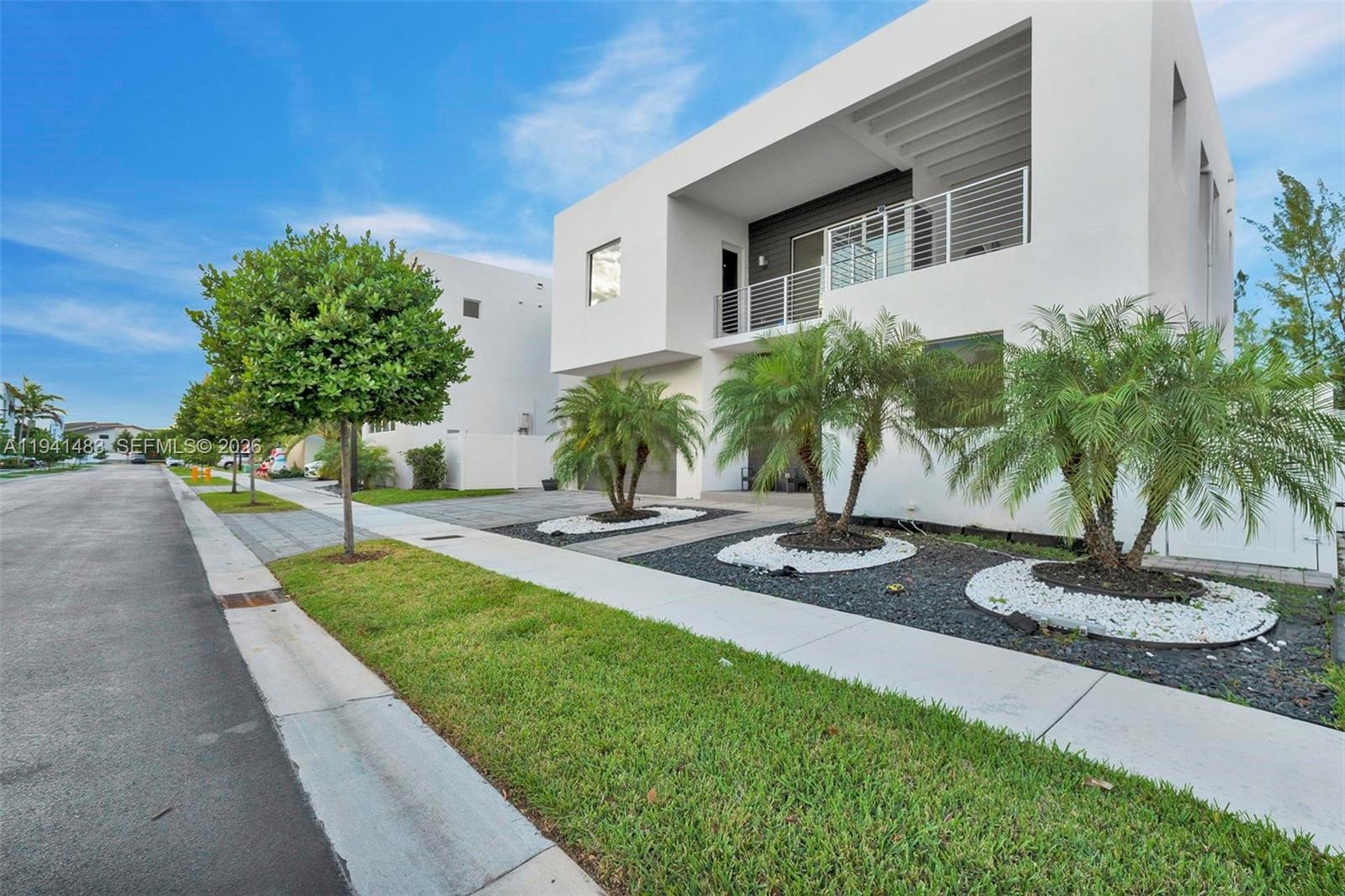 A modern two-story white house features a balcony, palm trees, and a landscaped front yard — 10055 NW 77th St, Doral FL 33178, DORAL, FL