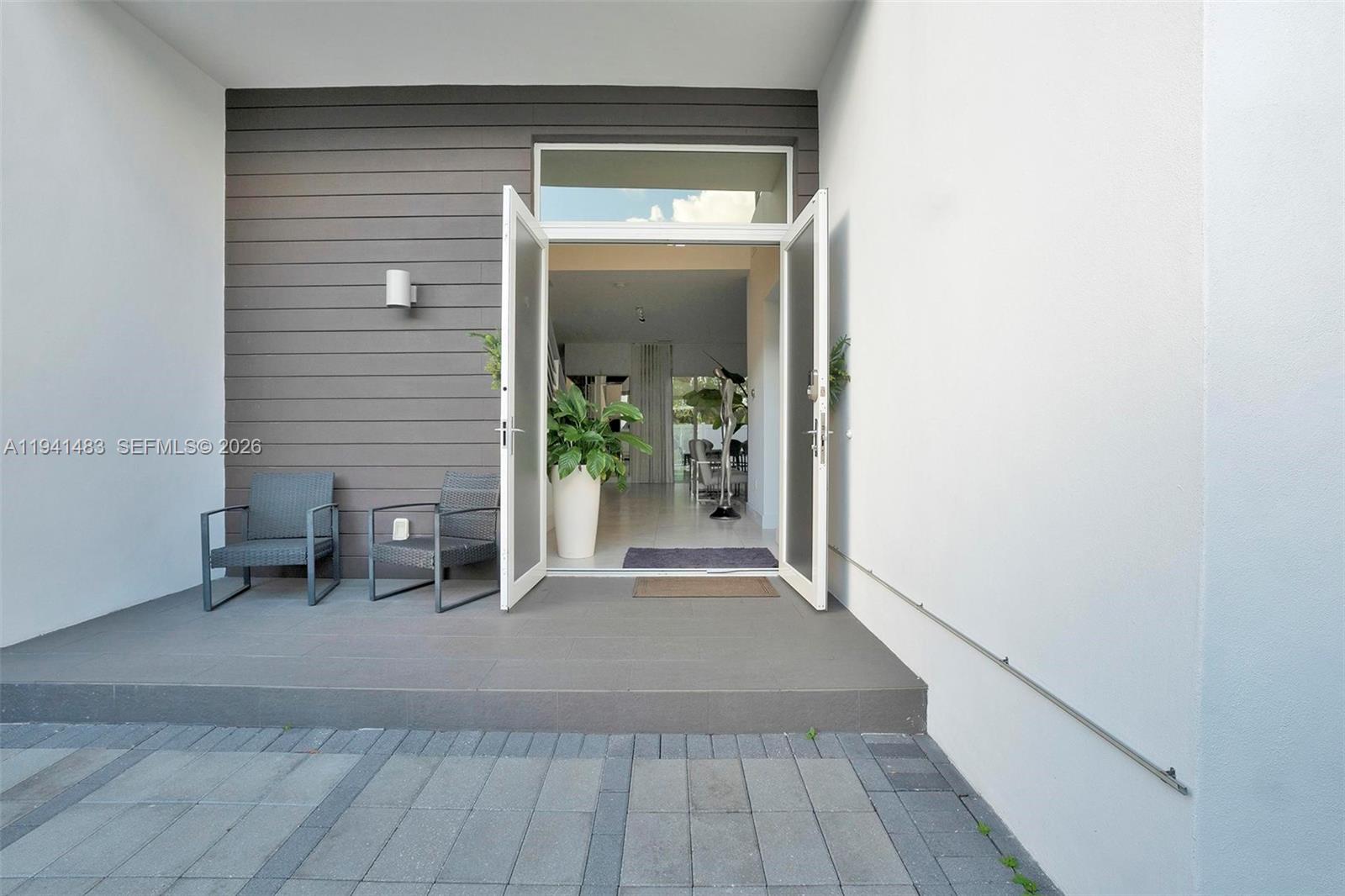 An outdoor patio with two chairs leads into a home through open glass doors — 10055 NW 77th St, Doral FL 33178, DORAL, FL