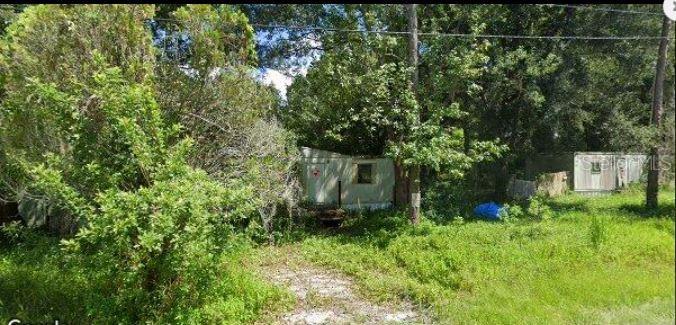 Two small, weathered mobile home structures sit on a grassy, wooded lot — 6927 AZLEE AVENUE, NEW PORT RICHEY, FL
