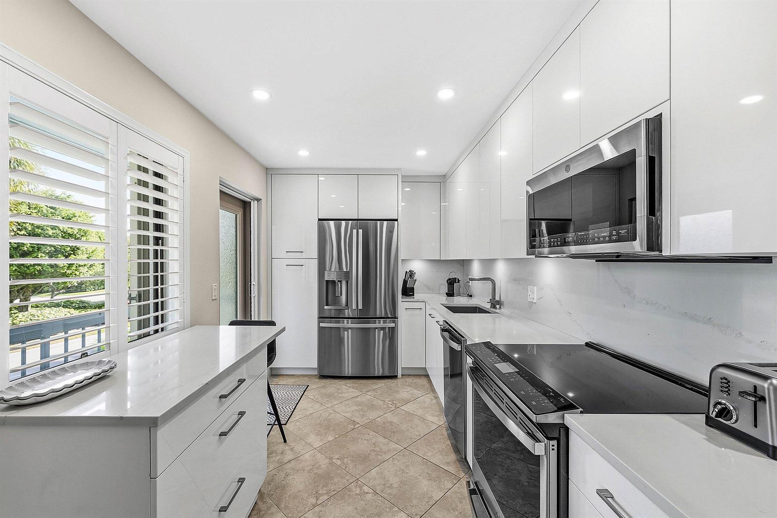 A modern kitchen features white glossy cabinets, stainless steel appliances, and a stone countertop island — 4114 B Quail Ridge Drive N, Boynton Beach FL 33436, BOYNTON BEACH, FL