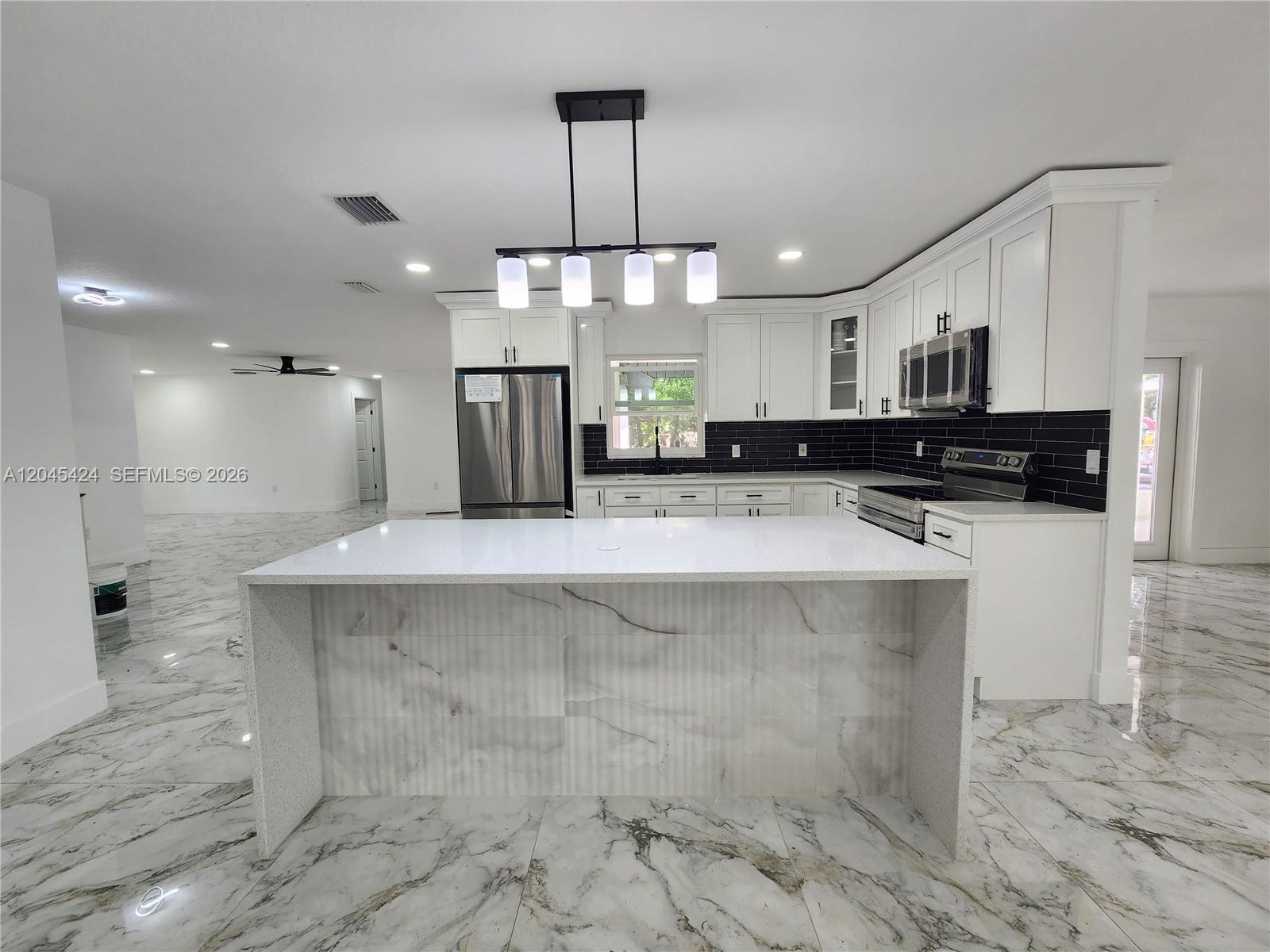A modern kitchen features white cabinets, a marble-topped island, and black subway tile backsplashes — 3133 Washigton Road, Brandon FL 33594, BRANDON, FL