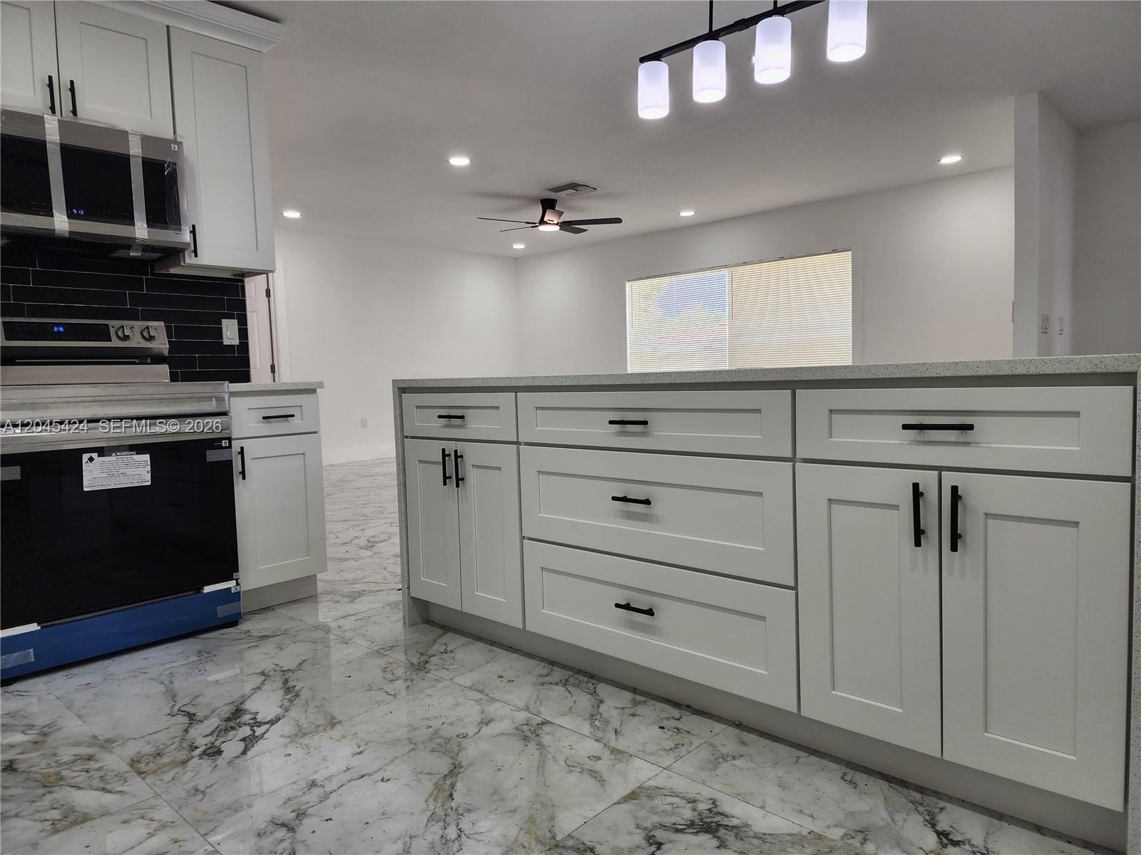 A kitchen features white cabinets, a marble-patterned floor, and a large central island — 3133 Washigton Road, Brandon FL 33594, BRANDON, FL